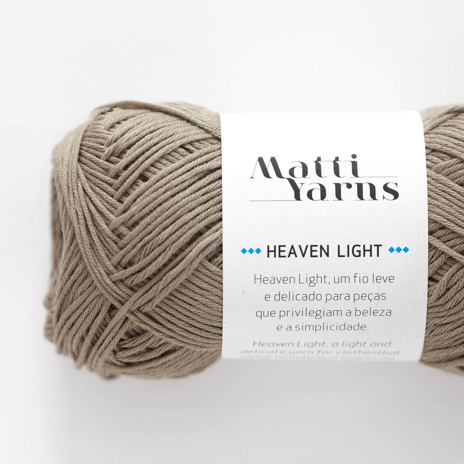 Novelo de fio bege claro da Matti Yarns com etiqueta Heaven Light em fundo branco.