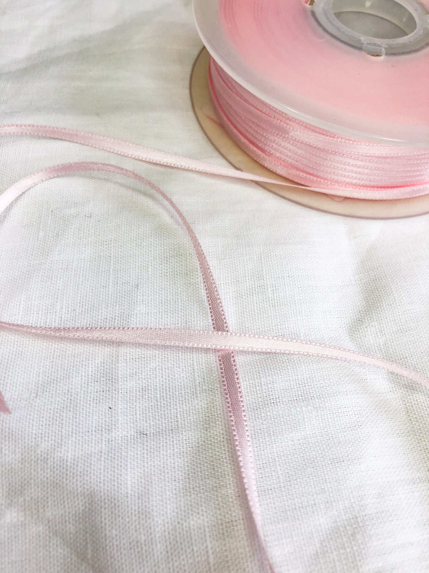 Fita rosa claro fina em carretel transparente sobre tecido branco