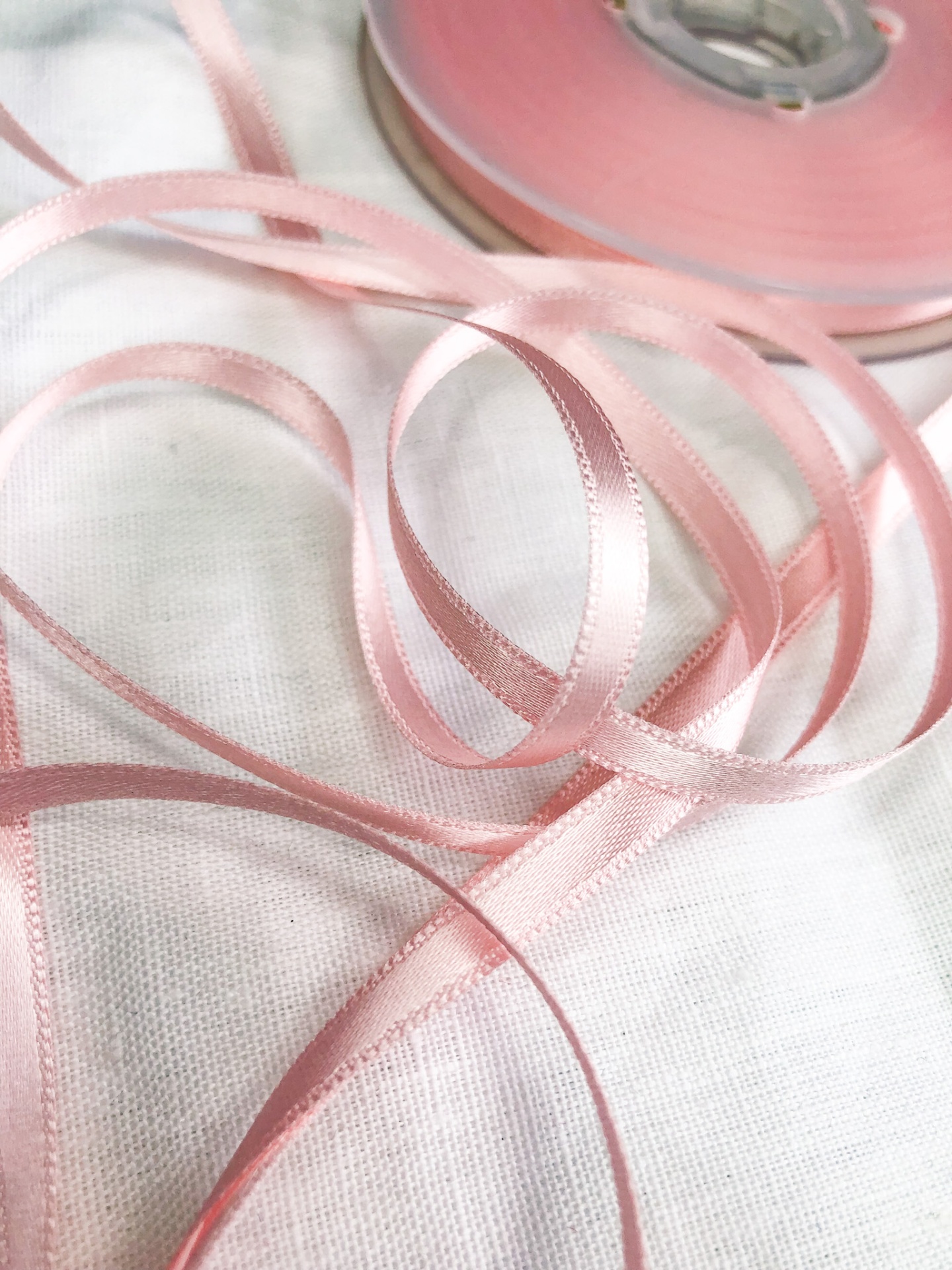 Fita de cetim cor-de-rosa clara fina enrolada em carretel transparente sobre tecido branco