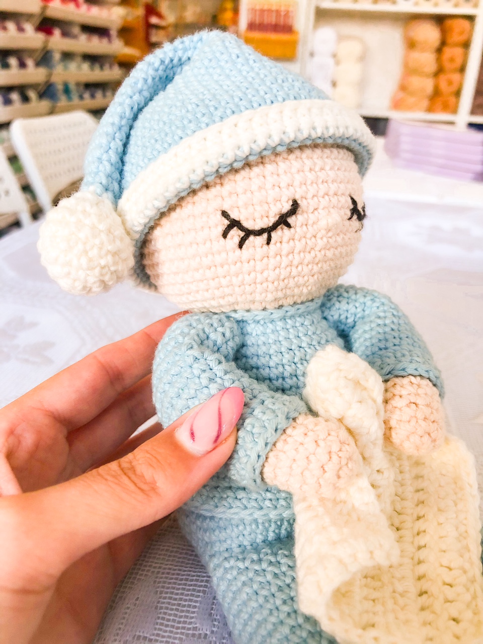 Boneco de croché azul e branco com manta branca e olhos fechados bordados