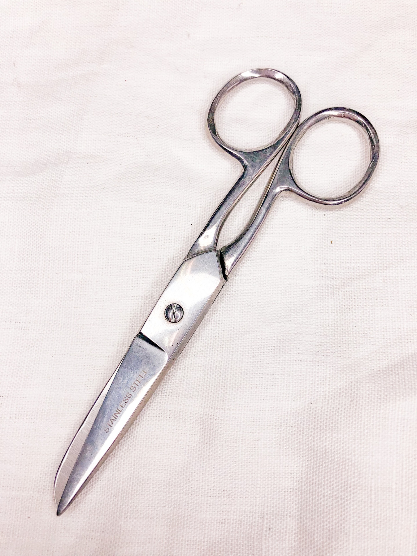 Tesoura pequena metálica com cabo arredondado sobre tecido branco