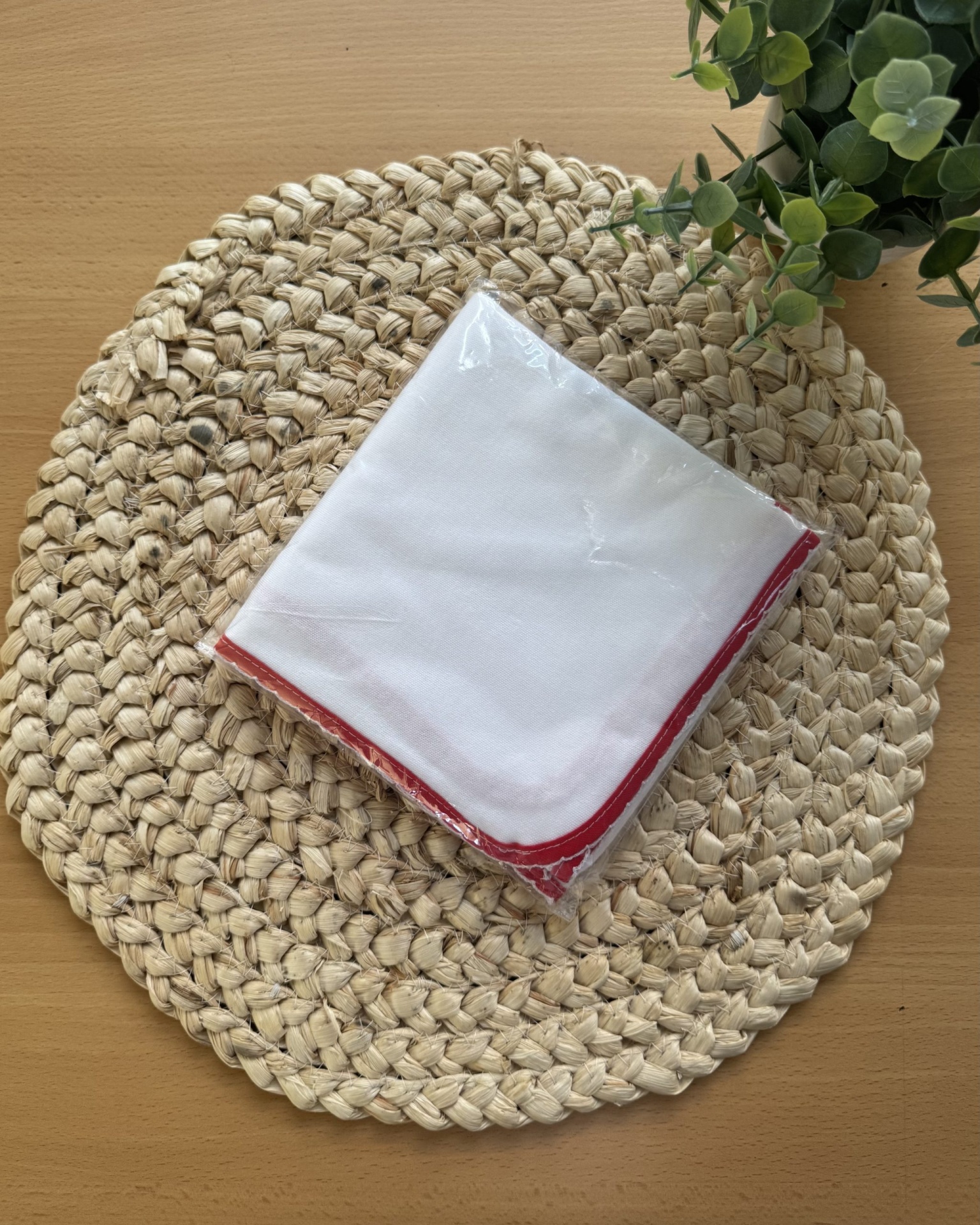 Guardanapo branco com borda vermelha sobre base de fibra natural numa mesa de madeira