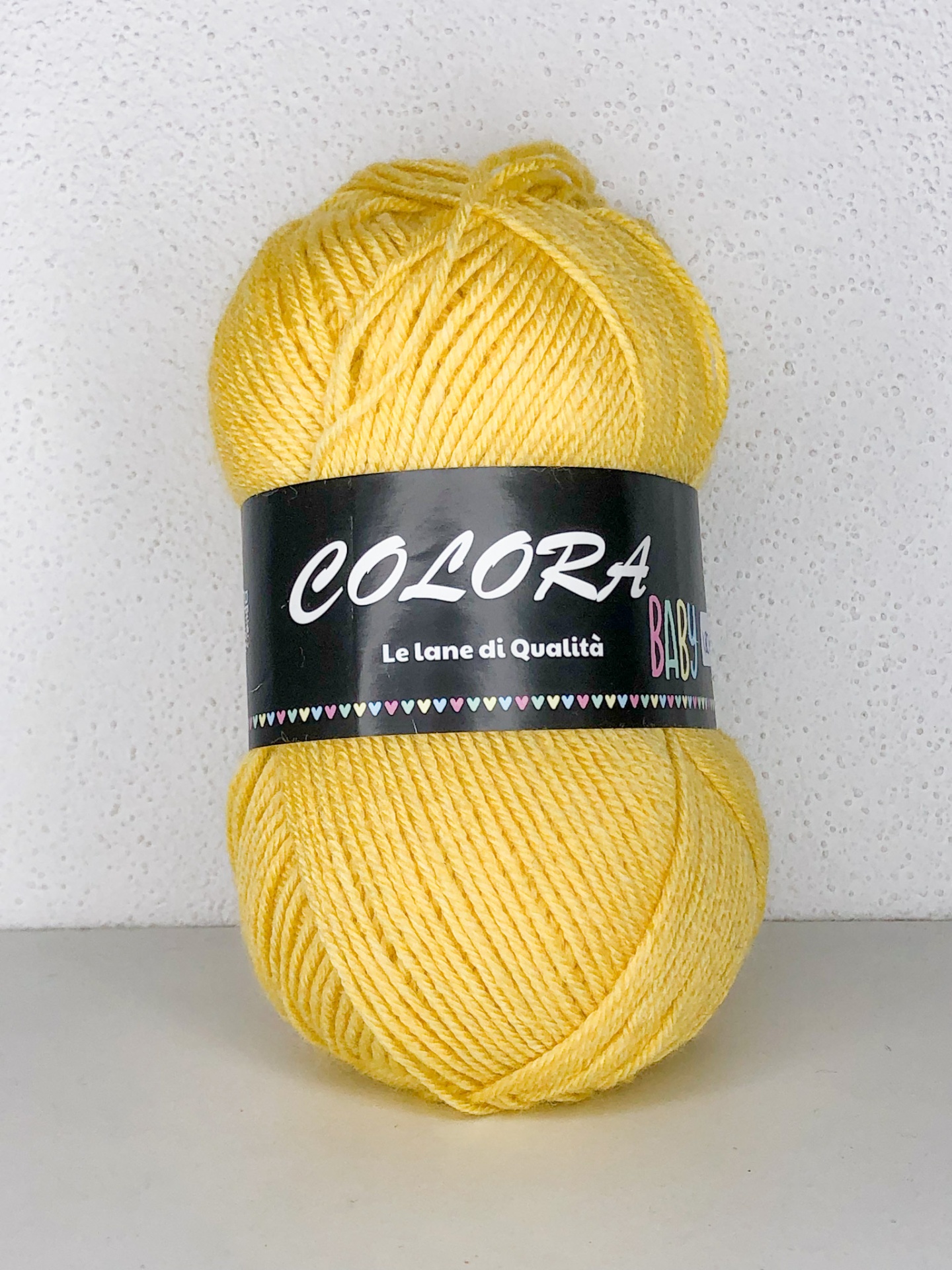 Novelo de lã amarelo com rótulo preto e texto COLORA Le lane di Qualità