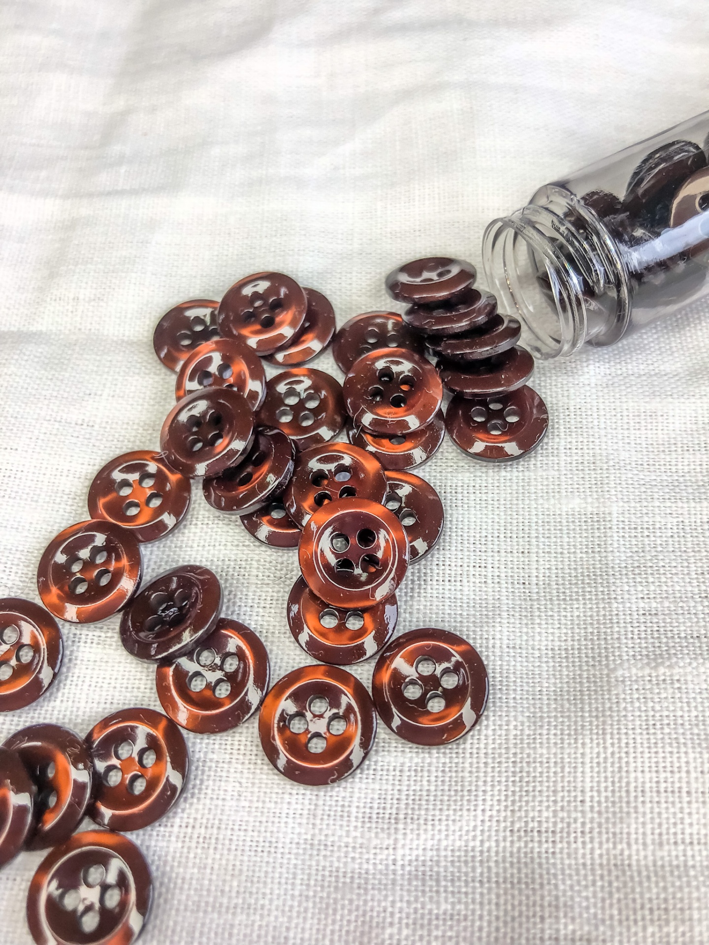 Botões castanhos translúcidos com quatro furos sobre tecido bege e garrafa plástica aberta
