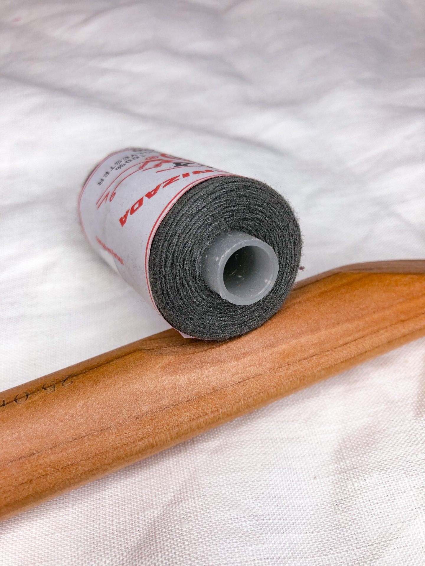Rolo de linha cinzenta com etiqueta vermelha sobre tecido branco e madeira clara