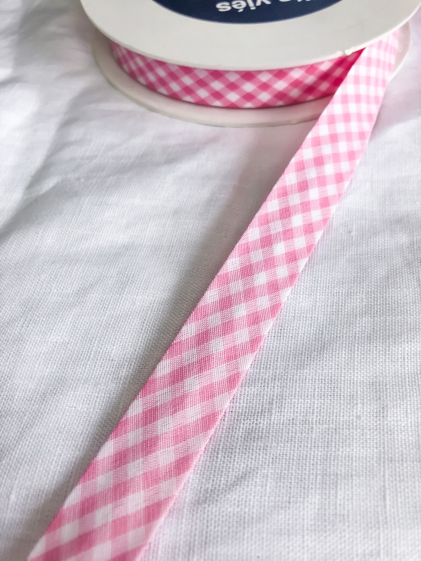 Fita de tecido xadrez rosa e branco numa bobina sobre tecido branco