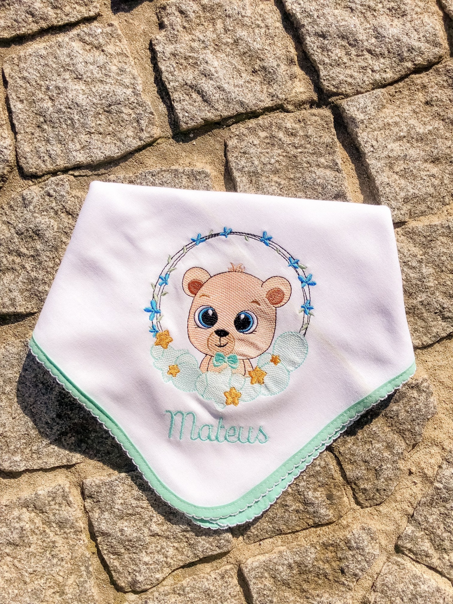 Babete branco com bordado de urso e nome Mateus em fundo de pedras