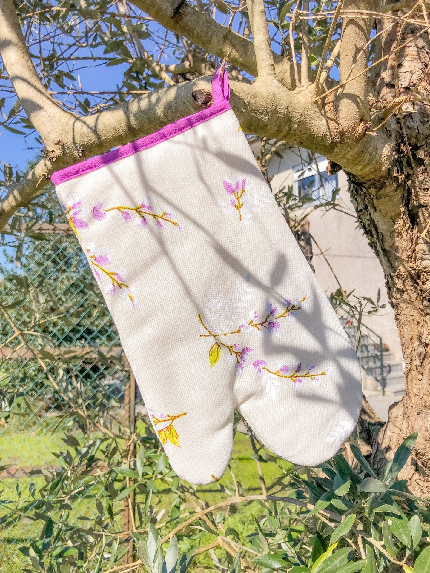 Luva de forno bordada branca com acabamento rosa pendurada numa árvore