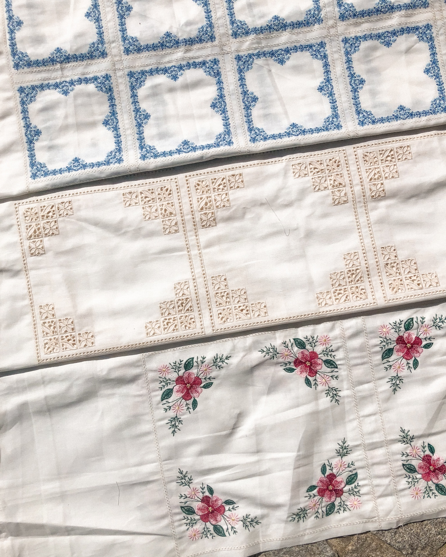 Panorama de três panos de mesa bordados com padrões em azul, bege e flores vermelhas e verdes.
