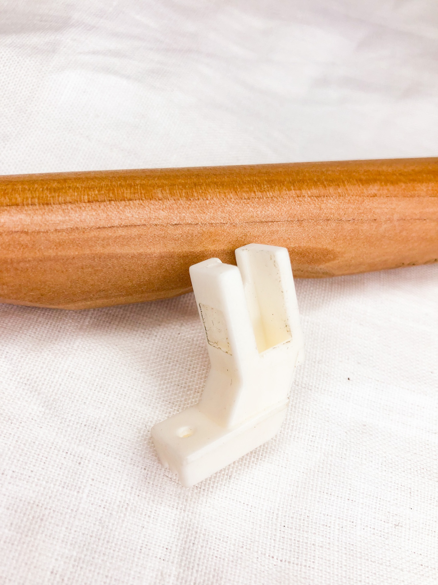 Peça plástica branca angular junto a superfície cilíndrica de madeira clara sobre tecido branco