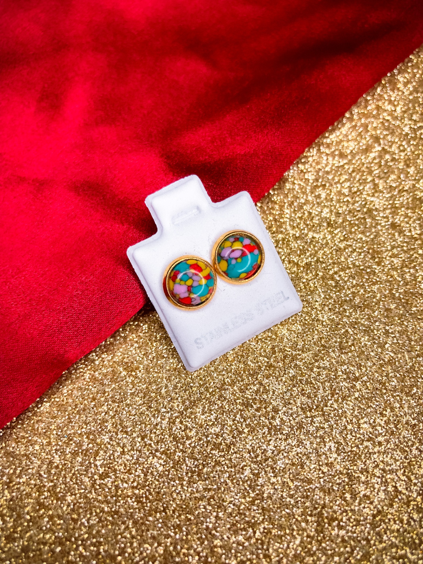 Brincos redondos coloridos Saint Laurent em suporte branco sobre fundo vermelho e dourado