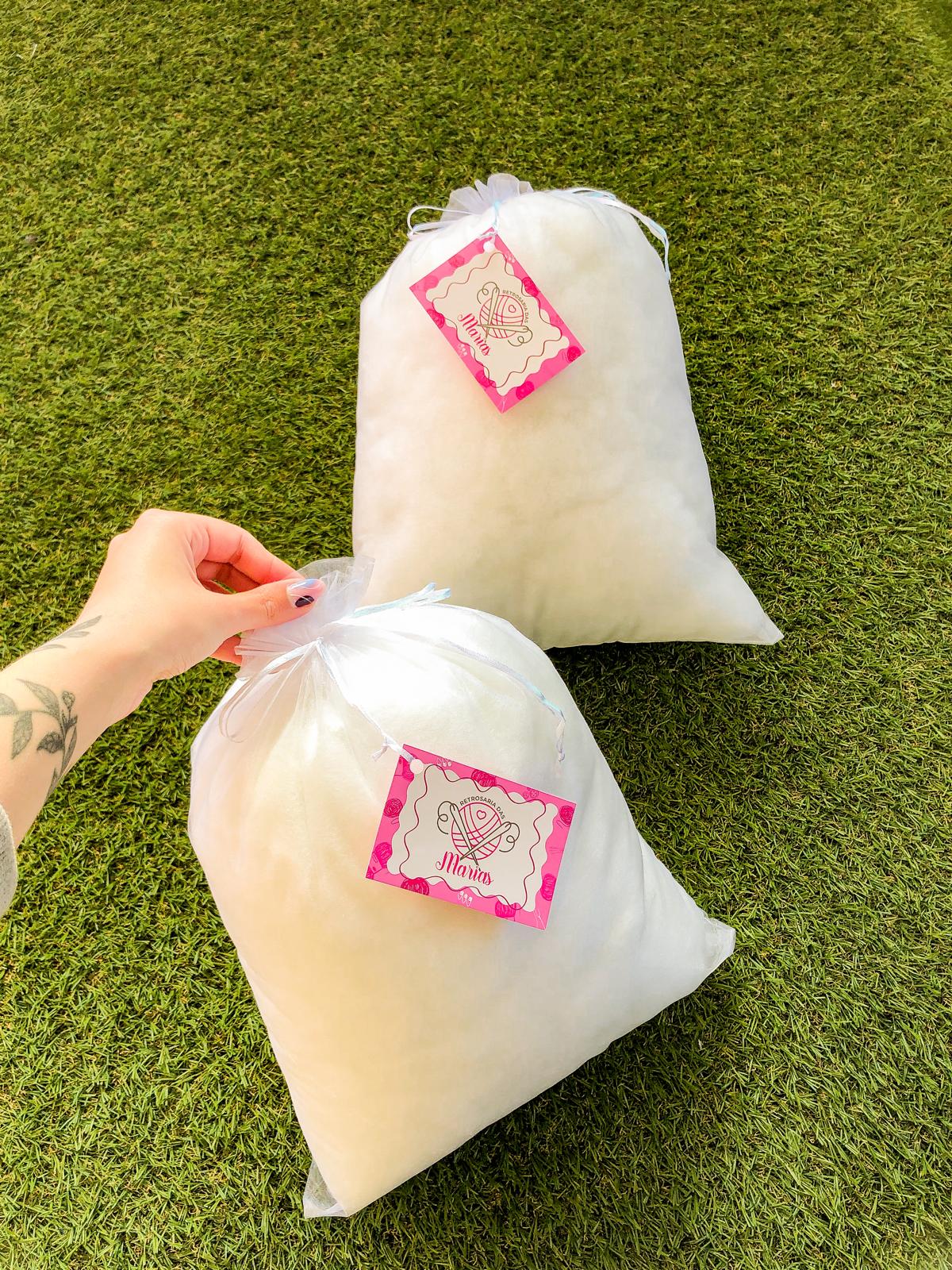 Duas almofadas brancas em saco transparente com etiquetas cor-de-rosa sobre relva artificial verde.