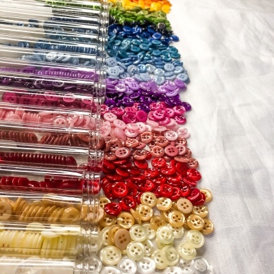 Botões pequenos redondos organizados por cor em recipientes transparentes sobre tecido branco