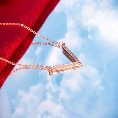 Colar dourado com pendente em V e pedras brilhantes sobre fundo vermelho e céu azul refletido