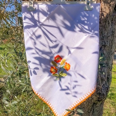 Pano branco bordado com flores coloridas pendurado numa árvore