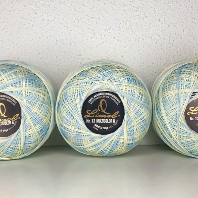 Três novelos de linha multicolor azul, branco e amarelo com rótulos pretos sobre superfície branca