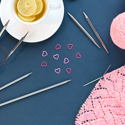 Materiais de tricô rosa, chá com limão, flores e agulhas sobre fundo azul.