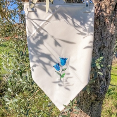 Toalha branca com bordado azul pendurada numa oliveira ao ar livre