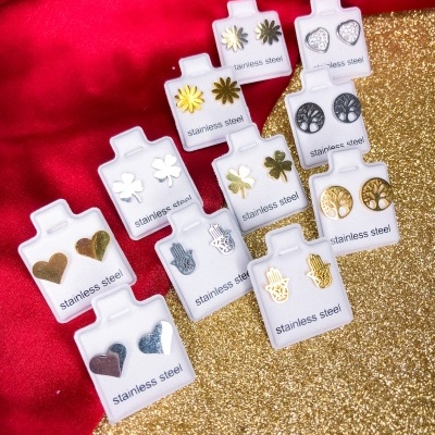 10 pares de brincos de aço inoxidável em suportes brancos sobre fundo vermelho e dourado