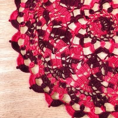 Toalha de mesa redonda em croché vermelho e castanho sobre madeira