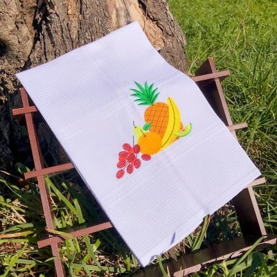 Toalha branca com bordado de frutas sobre armação de madeira, ao ar livre