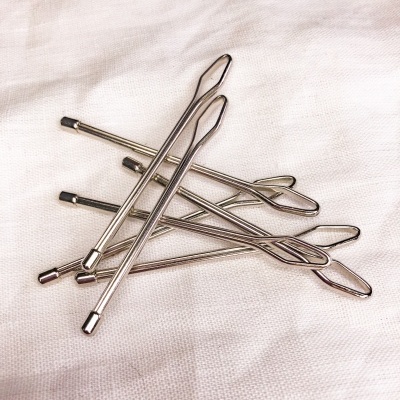 Cinco agulhas de costura metálicas prateadas sobre tecido branco