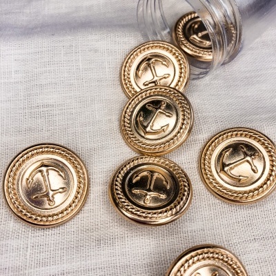 Botões dourados com âncora em frasco sobre tecido branco