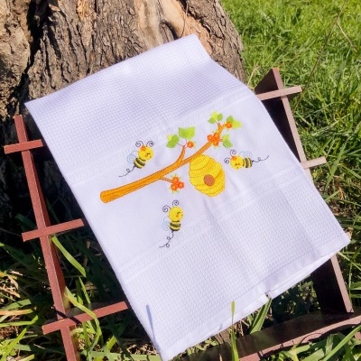 Toalha branca bordada com favo de mel e abelhas sobre estrutura de madeira na relva
