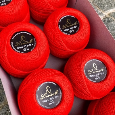 Novelos de fio vermelho Linhoel numa caixa rosa sobre cimento