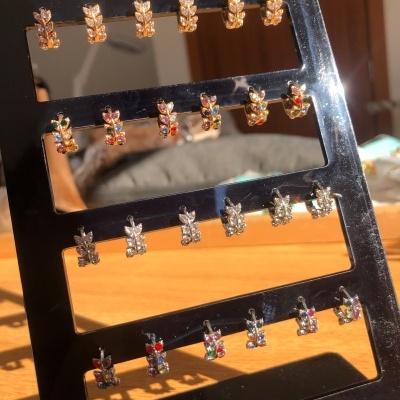 Expositor preto com 20 pares de brincos pequenos em metal dourado e prateado com pedras coloridas.