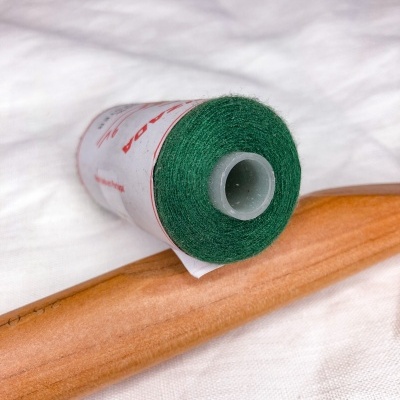 Rolo de linha verde com rótulo branco e vermelho, fita cola castanha, sobre tecido branco