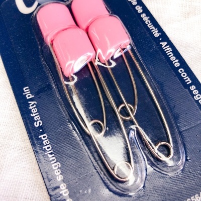 Conjunto de dois alfinetes de segurança rosa em embalagem azul