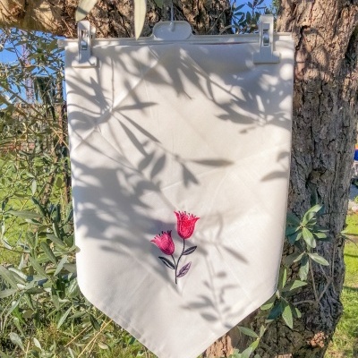 Pano branco com bordado de flores cor-de-rosa pendurado numa árvore