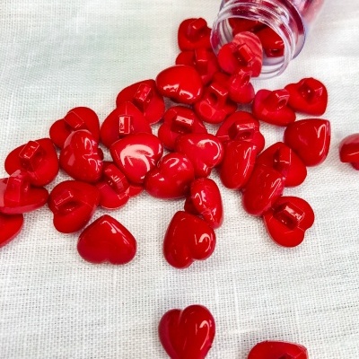 Contas vermelhas em forma de coração espalhadas sobre tecido branco com frasco transparente