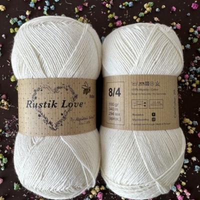 Dois novelos de lã branca Rustik Love com etiquetas castanhas e texto visível sobre composição e cuidados.