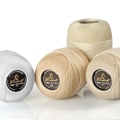 Quatro novelos de fio de algodão em branco e bege com rótulos pretos com texto dourado Sadovod.