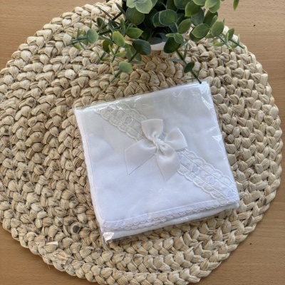 Guardanapo branco com renda e laço sobre suporte trançado com planta verde