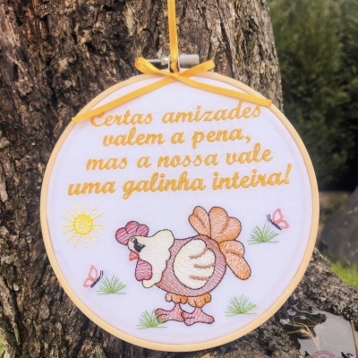 Bordado em bastidor com frase e desenho de galinha colorida pendurado em árvore