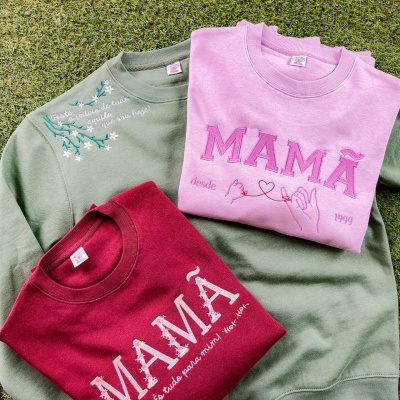 Três sweatshirts bordadas em verde, rosa e vinho em cima de relva