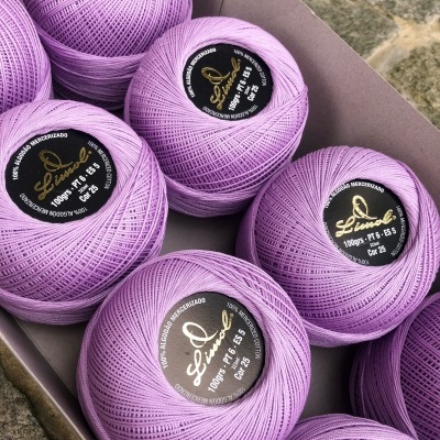 Bolas de linha lilás claro com etiquetas pretas e douradas numa caixa