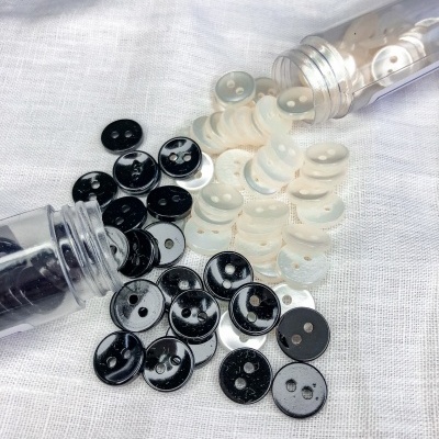 Botões pretos e brancos de plástico com dois furos sobre tecido branco