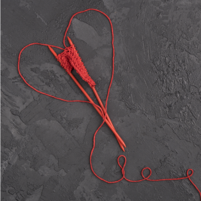 Agulhas de tricô vermelhas com fio formando a palavra 'love' e um coração em fundo cinza