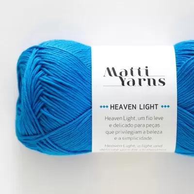 Novelo de fio azul com etiqueta Matti Yarns Heaven Light em fundo branco