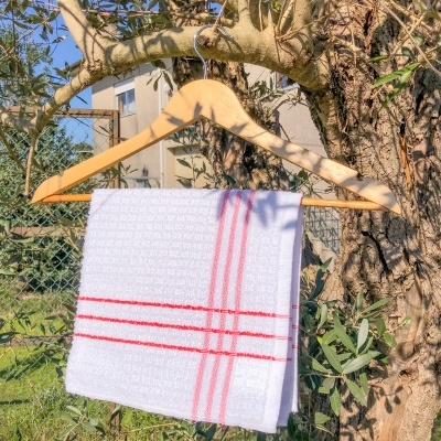 Toalha de cozinha branca com riscas vermelhas pendurada em cabide de madeira numa árvore