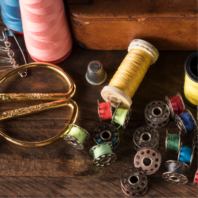 Carretéis de linha, tesouras douradas e dedal sobre mesa de madeira