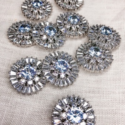 Botões decorativos prateados com pedras azuis sobre tecido bege