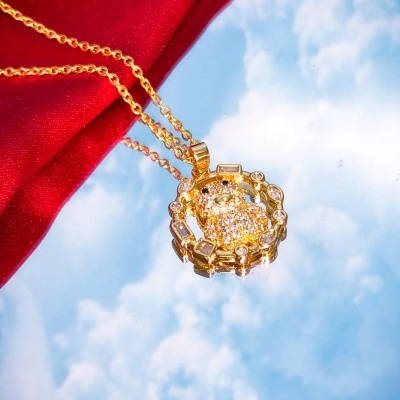 Colar dourado com pendente redondo com cristais sobre fundo de céu e tecido vermelho