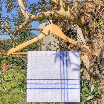 Toalha branca com riscas azuis pendurada num cabide de madeira numa árvore