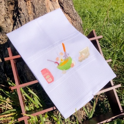 Toalha branca com bordado colorido disposta sobre estrutura de madeira em ambiente exterior