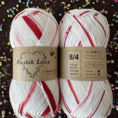 Dois novelos de fio de algodão branco com riscas vermelhas, rótulos castanhos, em fundo escuro com confetes coloridos